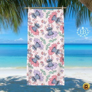 May include: A beach towel with a repeating pattern of a cartoon character in a flower design. The towel has a light pink background with blue, pink, and purple flowers, green leaves, and small mushrooms. The towel is hanging on a wooden rod.
