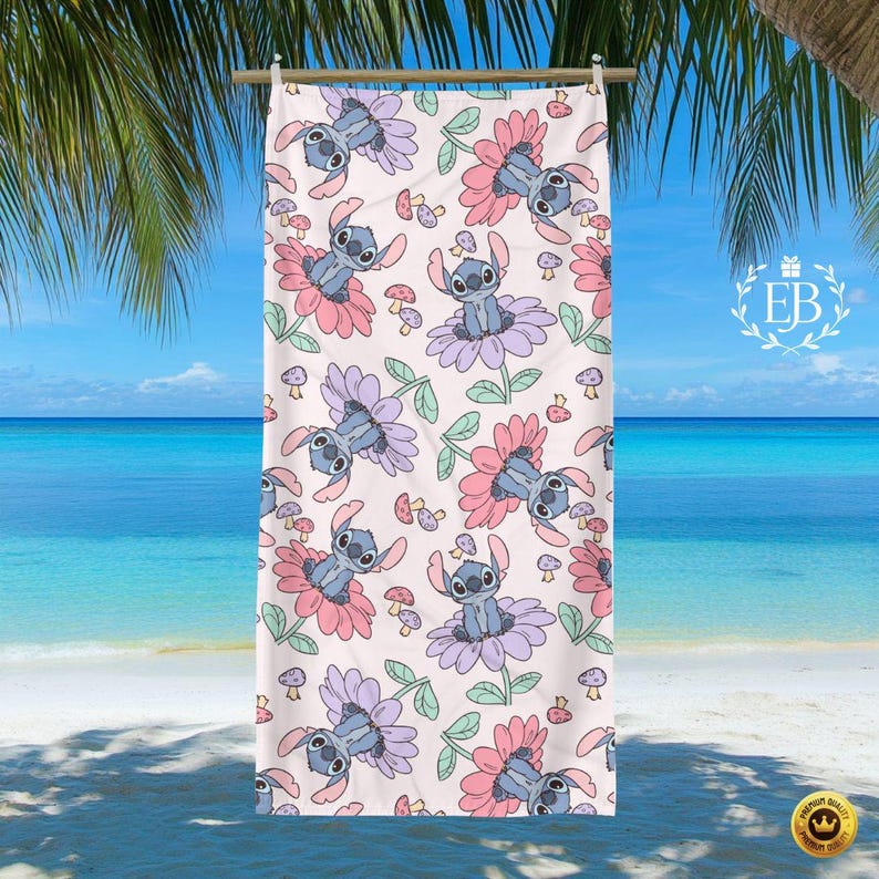 May include: A beach towel with a repeating pattern of a cartoon character in a flower design. The towel has a light pink background with blue, pink, and purple flowers, green leaves, and small mushrooms. The towel is hanging on a wooden rod.