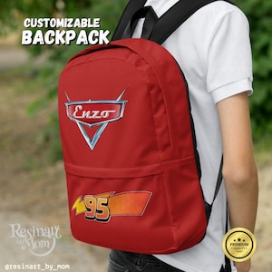 Puede incluir: Mochila roja con el texto "CUSTOMIZABLE BACKPACK" en la parte superior. La mochila presenta el logotipo "Enzo" y el n&uacute;mero "95" en un dise&ntilde;o tem&aacute;tico de carreras. La mochila la lleva una persona.
