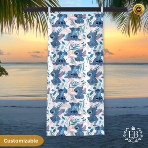 May include: A white beach towel featuring a repeating pattern of a blue cartoon character with large ears and a floral design in blue and pink. The word "Customizable" is printed on the bottom left.