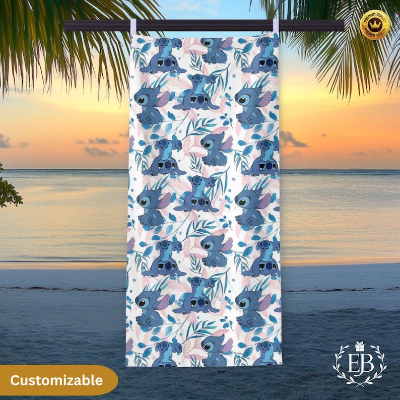 May include: A white beach towel featuring a repeating pattern of a blue cartoon character with large ears and a floral design in blue and pink. The word "Customizable" is printed on the bottom left.