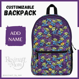May include: Purple backpack with a repeating pattern of green alien characters from the movie Toy Story. The backpack has a black zipper and a black handle. The text "ADD NAME" is on a purple background.