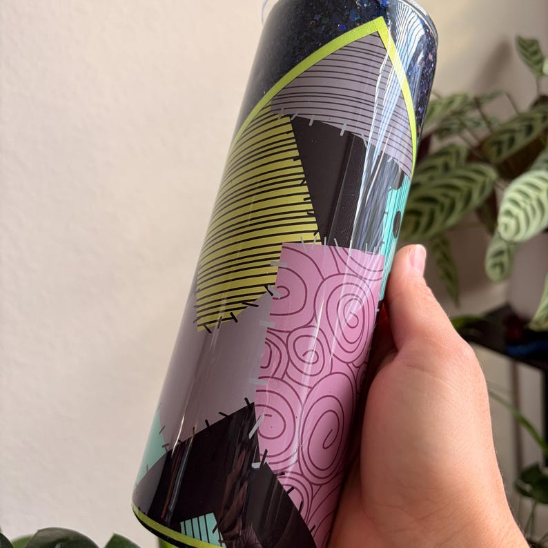 Puede incluir: Un vaso cil&iacute;ndrico con un dise&ntilde;o de patchwork colorido. El vaso presenta una mezcla de colores, incluyendo negro, gris, amarillo, rosa y turquesa. El dise&ntilde;o recuerda a un patr&oacute;n de tela cosida, con varias formas y l&iacute;neas.