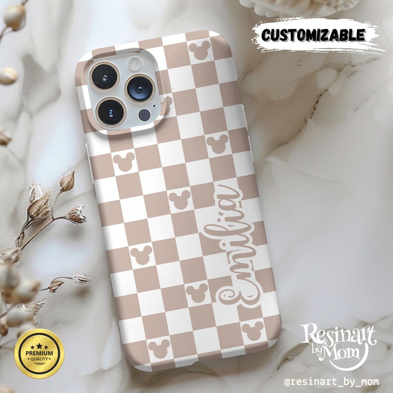 May include: A phone case with a tan and white checkered pattern and Mickey Mouse silhouettes. The word "Emilia" is written in a script font. The case is labeled "Customizable" and has a "Premium Quality" seal.