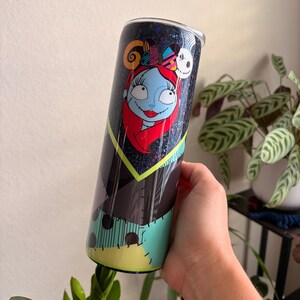 Puede incluir: Un vaso alto y aislado con un dise&ntilde;o de Sally de The Nightmare Before Christmas. El vaso tiene un fondo negro brillante y un dise&ntilde;o de patchwork colorido. El gr&aacute;fico de Sally incluye su piel azul, cabello rojo y una diadema con orejas de Mickey Mouse.
