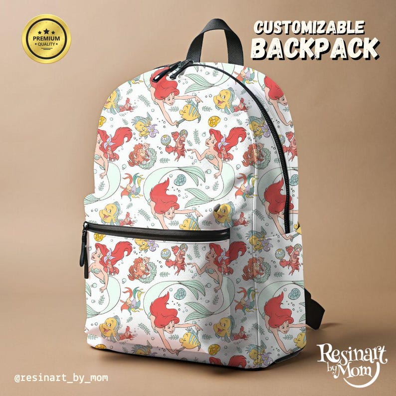 Puede incluir: Una mochila blanca personalizable con un patr&oacute;n repetido de Ariel, Sebasti&aacute;n y Flounder de La Sirenita. La mochila tiene correas y cremalleras negras. El texto "MOCHILA PERSONALIZABLE" est&aacute; en la esquina superior derecha de la imagen. El texto "Resinait by Mom" est&aacute; en la esquina inferior derecha de la imagen.