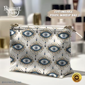May include: A white cosmetic pouch with a repeating pattern of blue and gold evil eye designs. The pouch has a gold zipper and the text "CUSTOMIZABLE POUCH, MAKEUP BAG". The brand name "Resinart by Mom" is also visible.