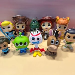May include: A collection of Toy Story character ornaments. The ornaments include Woody, Buzz Lightyear, Jessie, and others. Each ornament has a silver loop for hanging and is brightly colored.