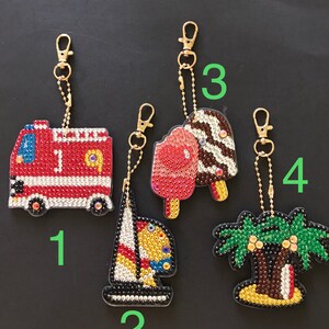 May include: Four colorful keychains with different designs: a red fire truck, a sailboat, a pink and brown ice cream cone, and a green palm tree. Each keychain has a gold chain and a gold clasp.