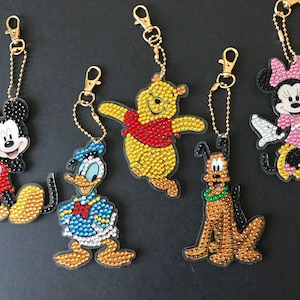 May include: Six colorful Disney character keychains featuring Mickey Mouse, Minnie Mouse, Donald Duck, Winnie the Pooh, Goofy, and Pluto. Each keychain is made of clear plastic with a rhinestone design.