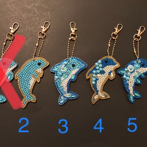 May include: Five dolphin keychains with blue and white diamond-shaped rhinestones. The keychains are numbered 1 through 5.