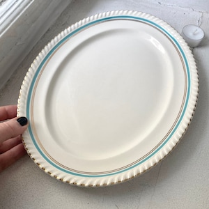 Op de afbeelding: Een witte ovale serveerschaal met een gouden en lichtblauwe rand. De schaal heeft een touwachtig ontwerp rond de rand.