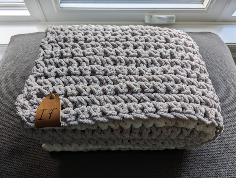 May include: A soft, gray and white crocheted throw blanket with a brown leather tag that says "IF".