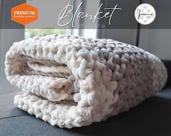 May include: A soft, beige and brown crocheted blanket with a fluffy texture. The blanket is folded and measures 27 inches by 57 inches. The text "Blanket" and "27 in x 57 in" is visible on the image.