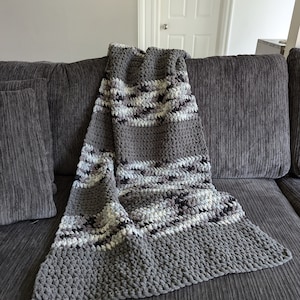 May include: A gray and white striped crocheted throw blanket with a textured, fluffy surface. The blanket is draped over a gray couch.
