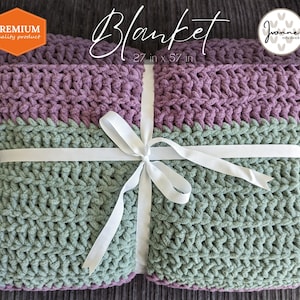 K&ouml;nnte beinhalten: Eine geh&auml;kelte Decke in Gr&uuml;n und Lila, die mit einem wei&szlig;en Band gebunden ist. Die Decke ist 27 Zoll mal 57 Zoll gro&szlig;. Der Text "Blanket" und "27 in x 57 in" ist auf einem wei&szlig;en Etikett aufgedruckt.