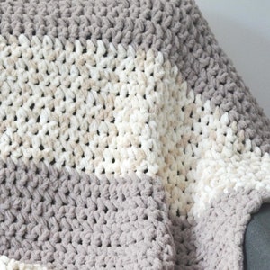 May include: A soft, cozy blanket with a striped pattern in shades of gray and beige. The blanket is made of a fluffy, textured yarn and is perfect for snuggling up on the couch.