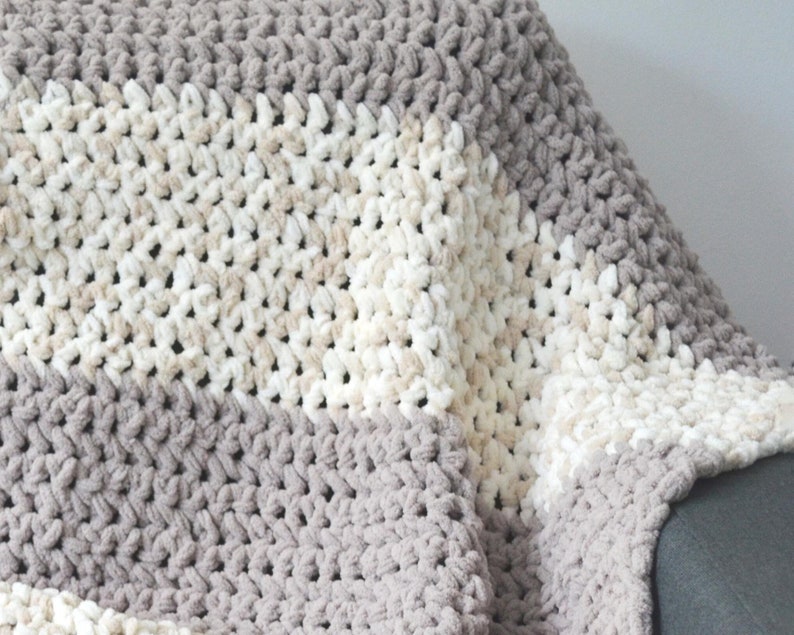 May include: A soft, cozy blanket with a striped pattern in shades of gray and beige. The blanket is made of a fluffy, textured yarn and is perfect for snuggling up on the couch.