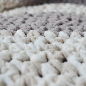 May include: Close-up of a soft, textured bath mat with a beige and white color scheme. The mat has a raised, looped design.