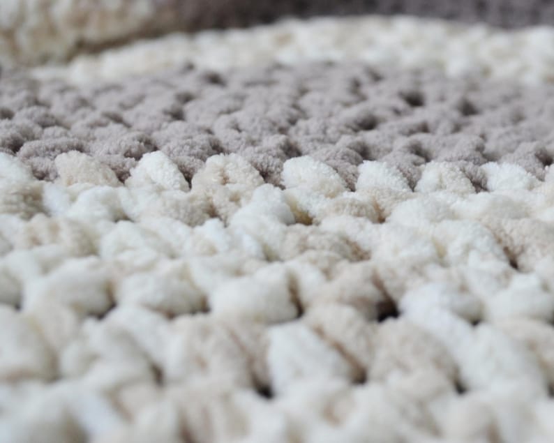 May include: Close-up of a soft, textured bath mat with a beige and white color scheme. The mat has a raised, looped design.