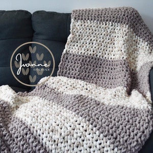 May include: A gray and white striped crocheted throw blanket draped over a gray couch. The blanket is made with thick yarn and has a chunky texture. The blanket is handmade and has a tag that says "Yvonne Handmade".