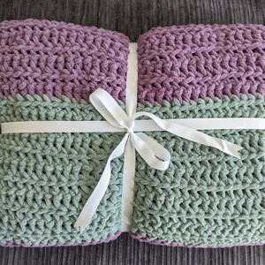 May include: A green and purple crocheted throw blanket tied with a white ribbon.