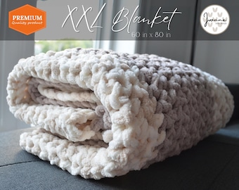 May include: A large, cream and brown crocheted blanket folded on a gray couch. The blanket is labeled "XXL Blanket 60 in x 80 in".