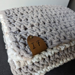 May include: A gray and white crocheted blanket with a brown leather tag that says "IF".