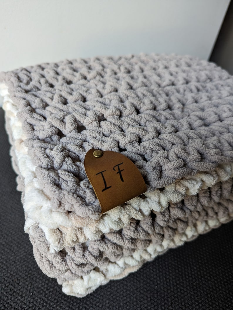 May include: A gray and white crocheted blanket with a brown leather tag that says "IF".