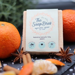 Könnte beinhalten: Eine natürliche Salzseife mit einem Etikett, auf dem "The Soap Bros Natural Soap Est. 2020" und "Naturliche Salzseife 100g (BODY)" steht. Die Seife ist von Orangenscheiben, Zimtstangen und Sternanis umgeben.