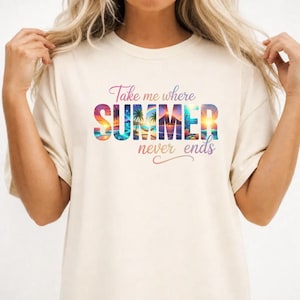May include: A cream-colored short-sleeve t-shirt featuring the text "Take me where SUMMER never ends" in a cursive and block font. The word "SUMMER" is filled with a colorful graphic of a tropical beach scene with palm trees and a sunset.