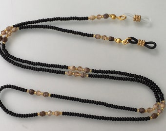 Könnte beinhalten: Schwarze und braune Perlen-Brillenschnur mit goldfarbenen Metallverschlüssen. Die Schnur besteht aus kleinen Perlen und hat ein Doppelfaden-Design.