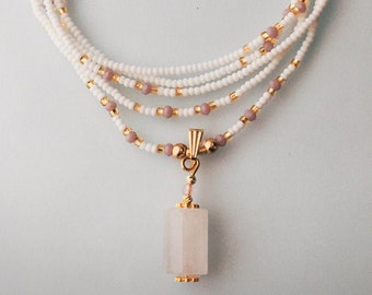 Op de afbeelding: Een witte en lichtroze kralenketting met een gouden ketting en een rechthoekige witte stenen hanger.