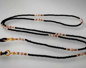 Könnte beinhalten: Schwarze Perlen-Brillenschnur mit goldenen und rosafarbenen Akzenten. Die Schnur hat zwei schwarze Gummieenden mit goldenen Akzenten.