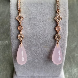 May include: A pair of rose gold earrings with a teardrop-shaped pink stone, a round clear stone, and a square clear stone.