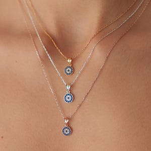 May include: Three delicate necklaces with small, round pendants. Each pendant features a blue and white design, possibly an eye or a similar motif. The necklaces are gold, silver, and rose gold in color, and are layered for a stylish look.