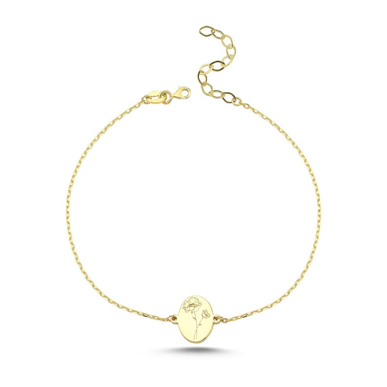 Puede incluir: Una pulsera de cadena en tono dorado con un colgante central de forma ovalada. El colgante est&aacute; grabado con un delicado dibujo lineal de una flor. La pulsera incluye una cadena de eslabones finos y un cierre de mosquet&oacute;n con cadena extensible.