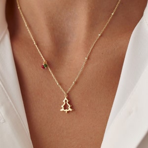 May include: A delicate gold necklace featuring a Christmas tree pendant. The necklace has a fine chain with small beaded accents and a small cluster of red and green beads near the clasp. The tree pendant is a simple, open design.