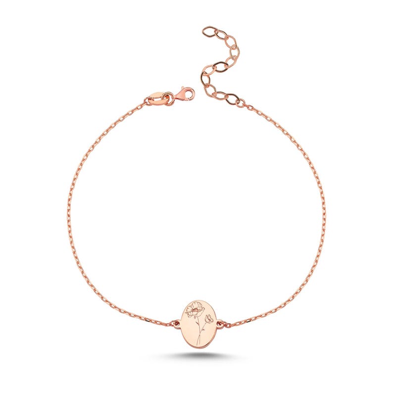 Puede incluir: Una pulsera de cadena en tono oro rosa con un dije ovalado central grabado con un delicado dibujo lineal de una flor de amapola. La pulsera incluye una cadena fina de eslabones con cierre de mosquet&oacute;n y una cadena extensora ajustable.