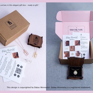 May include: A brown cardboard gift box with the Dabas Minimalist logo, containing jewelry, a wooden display case, and informational cards. The open box interior is light pink with a Thank You note, and a gold necklace with a letter M pendant.