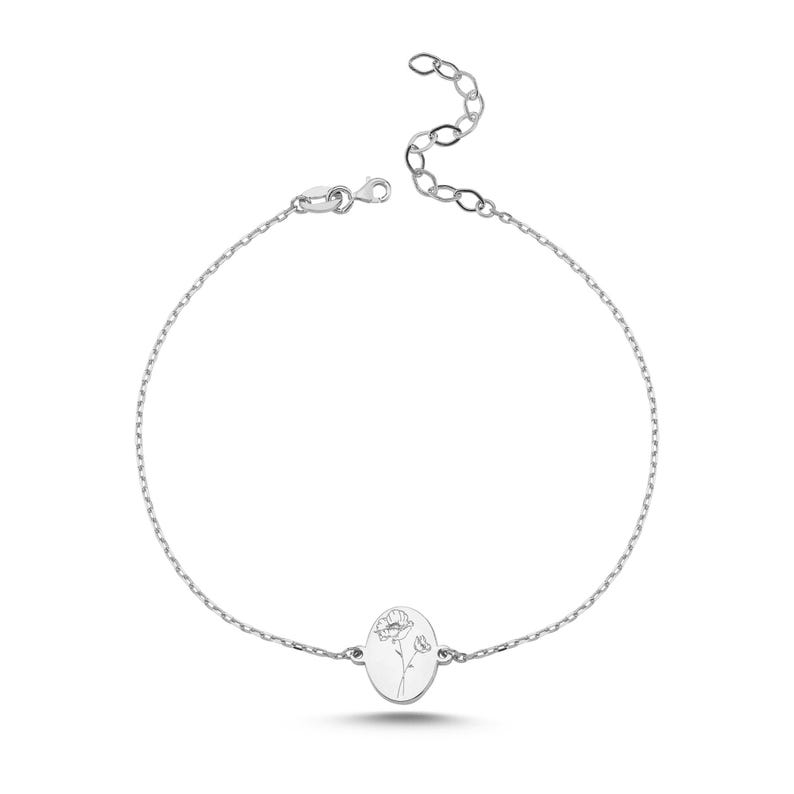 Puede incluir: Una pulsera de cadena en tono plateado con un dije central de forma ovalada. El dije presenta un delicado grabado de una flor de amapola. La pulsera incluye una cadena de eslabones finos y un cierre de mosquet&oacute;n con extensi&oacute;n.