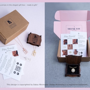 Puede incluir: Una caja de regalo de cart&oacute;n marr&oacute;n con el logotipo de Dabas Minimalist, que contiene joyas, un estuche de madera y tarjetas informativas. El interior de la caja abierta es rosa claro con una nota de agradecimiento y un collar dorado con una letra M.