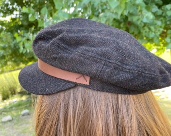 Fisherman's cap composed of herringbone pattern wool blend fabric. Faux leather band with side stitch detail