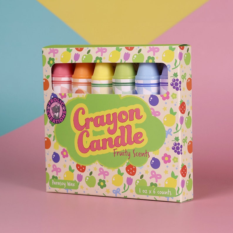 May include: A box of six crayon candles with fruity scents. The box is decorated with a colorful pattern of fruits, flowers, and stars. The candles are made of parsoy wax and are 1 oz each.