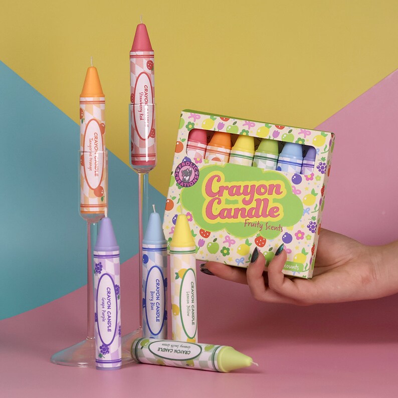 May include: A set of crayon-shaped candles in a box with a colorful design. The candles are labeled with different fruit scents, including strawberry, tangerine, lemon, berry, and grape. The box says "Crayon Candle" and "Fruity Scents".