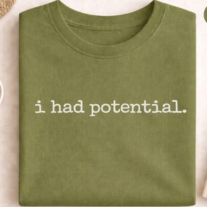 Pode incluir: Uma caneca de cerâmica branca com uma alça preta e o texto "But First, Coffee" em preto, em negrito. A caneca está sobre uma superfície branca.