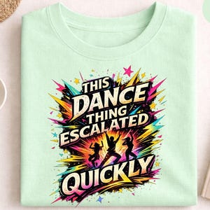 May include: A mint green sweatshirt featuring the phrase "THIS DANCE THING ESCALATED QUICKLY" in a colourful, graphic design. The design includes dancing figures and starbursts. A fun and vibrant apparel item.