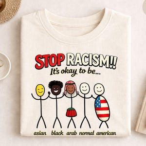 Może przedstawiać: Kremowa koszulka z napisem "STOP RACISM!! It's okay to be..." w kolorze czerwonym i czarnym. Grafika przedstawia ludziki reprezentujące różne grupy etniczne, z napisami takimi jak "asian", "black" i "american".