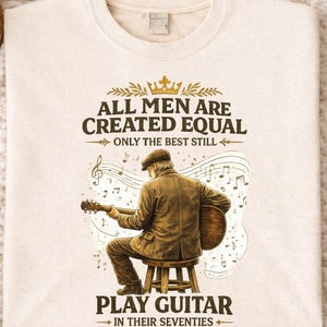 Peut inclure: Sweat-shirt crème avec le texte "ALL MEN ARE CREATED EQUAL ONLY THE BEST STILL PLAY GUITAR IN THEIR SEVENTIES." Le graphisme montre un homme jouant de la guitare. Le t-shirt est entouré d'objets décoratifs.
