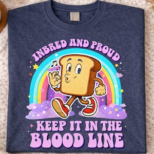 May include: Navy blue t-shirt featuring a cartoon bread slice character walking in front of a rainbow. The text reads "INBRED AND PROUD" above and "KEEP IT IN THE BLOOD LINE" below the bread character.